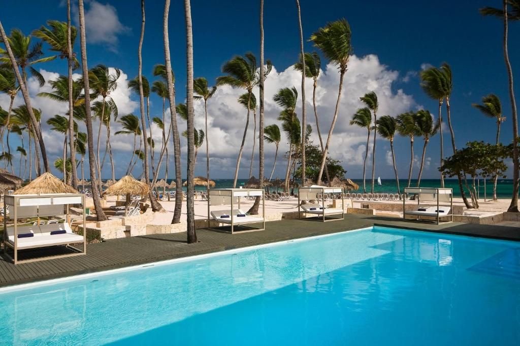 Piscina frente a la playa con camas balinesas y palmeras